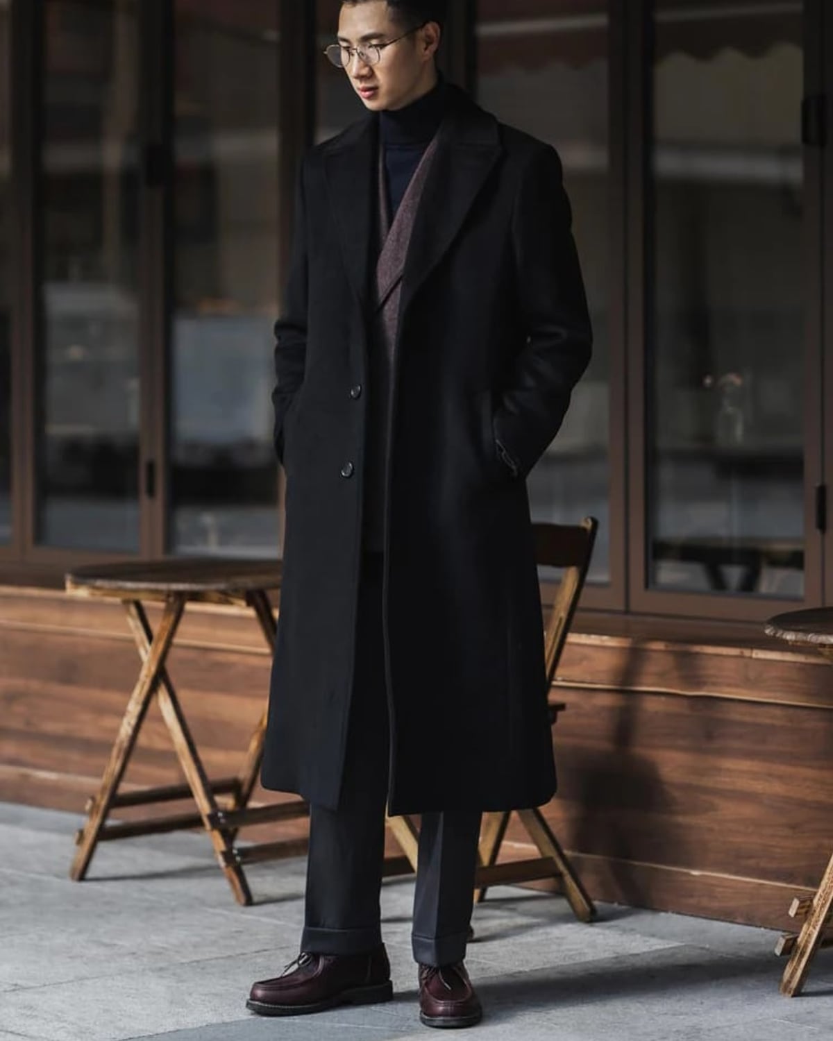 Man in a long black overcoat outside a cafe