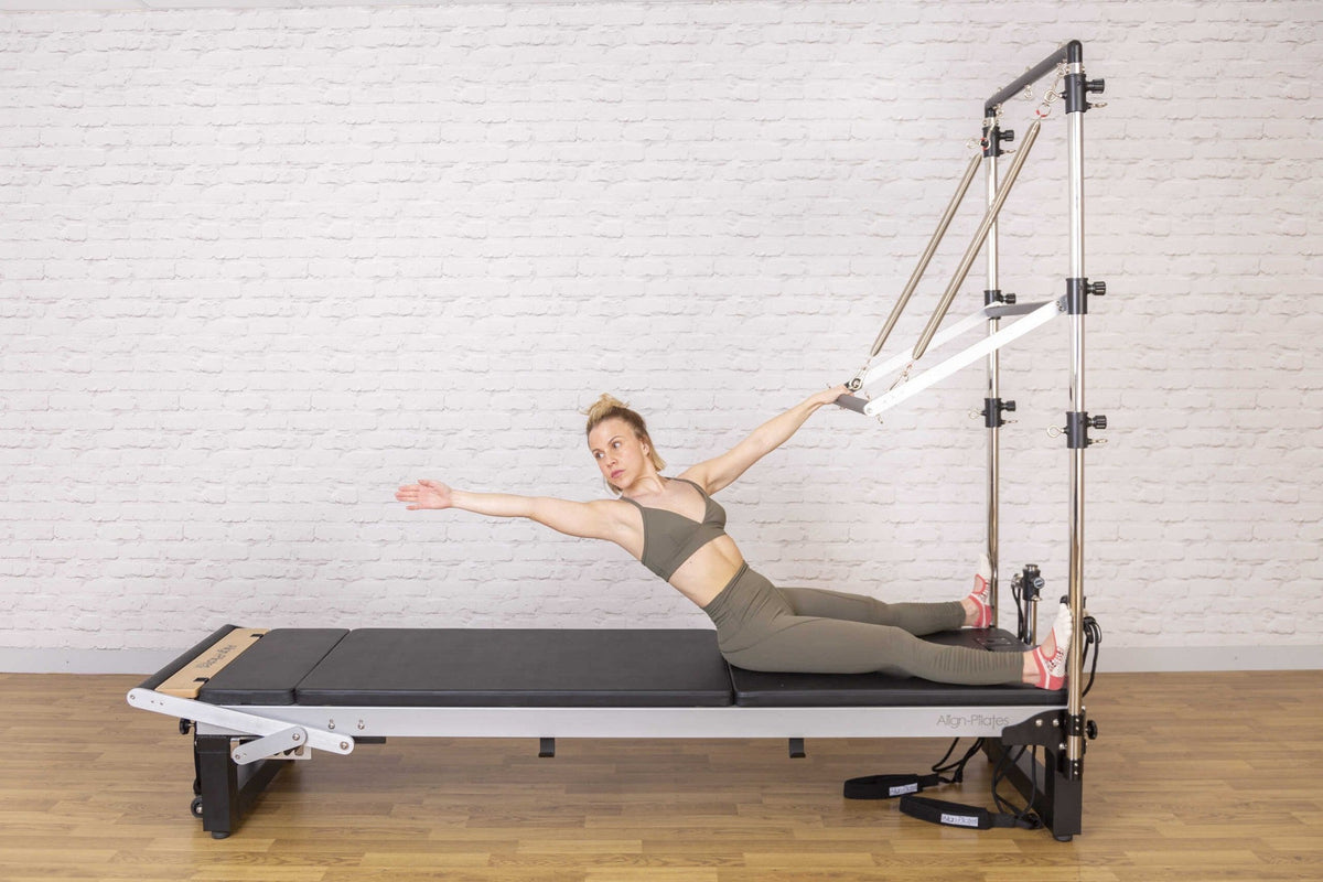 Align Pilates Half Cadillac Frame, woman seated on the bed reaching for the bar