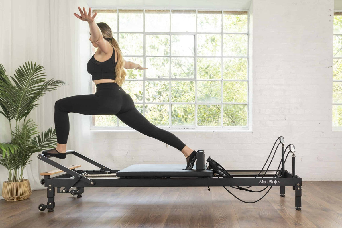 Align Pilates R8-Pro Reformer, woman in a standing lunge on the black frame