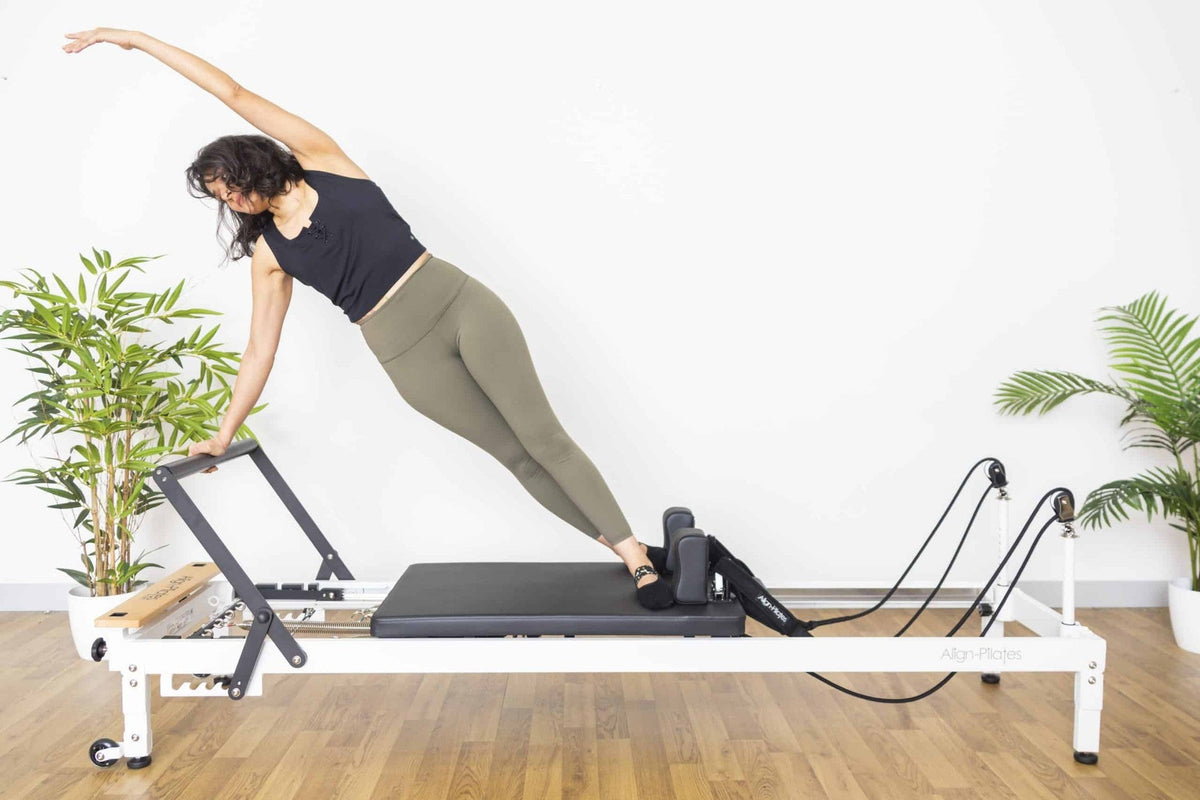 Align Pilates R8-Pro Reformer, woman doing a side stretch on the white frame